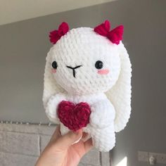 a hand holding a small white stuffed animal with a heart on it's chest