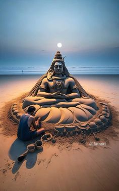 a man sitting on top of a sandy beach next to a giant buddha statue in the sand