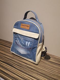 "Denim Backpack. From daily life to commuting to work, this Denim Backpack has your back. A large zipped compartment offers room for books and an extra slot for keeping your laptop secure. There is an exterior pocket that is clipped by two buttons in the front to help keep electronics and small essentials stored. As well the bag has two smaller pockets on either side to keep smaller items. Product Size: Width 13cm (5\"), Length 25cm (10\"), Height 30cm (12\")." Denim Backpack For Everyday And Back To School, Everyday Denim Backpack For Back To School, Travel Denim Backpack, Everyday Denim Standard Backpack, Daily Denim Backpack, Denim Blue Standard Backpack With Zipper, Denim Backpack For Back To School, Denim Travel Backpack, Denim Blue Backpack With Zipper Closure