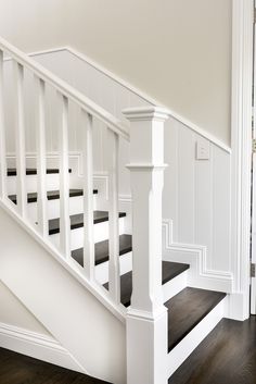 a white staircase with black carpet and wooden handrails in an empty room on the first floor