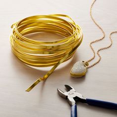 a pair of pliers next to some gold colored bracelets on a white table