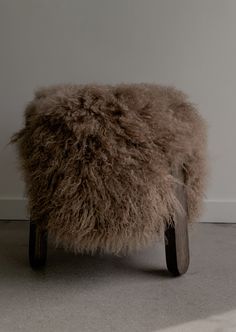 a sheepskin footstool sitting in front of a white wall on the floor