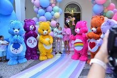 a group of people standing in front of a bunch of teddy bears on a rainbow colored carpet