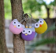 three crocheted key chains hanging from a tree trunk with two owls on them