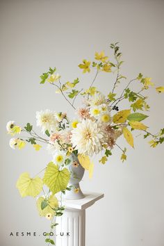 a vase filled with lots of flowers on top of a white table next to a wall