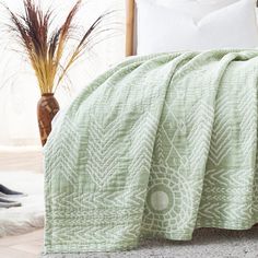 a bed covered in a green blanket next to a vase with dried grass on it