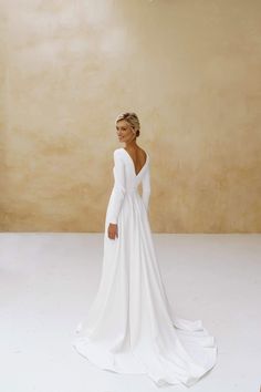 a woman in a white wedding dress standing against a wall with her back to the camera