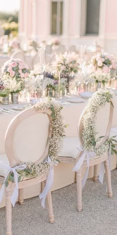 a table set up for a wedding with flowers and greenery on the back chairs