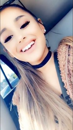 a woman with long hair wearing a black choker and smiling at the camera while sitting in a car