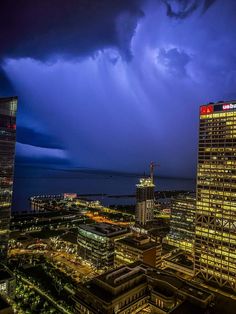 the city skyline is lit up with bright lights and dark clouds in the sky above