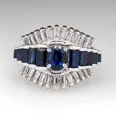 This captivating ring is centered with one (1) oval mixed cut natural sapphire set into a four-prong head. The ring is also accented with ten (10), channel set, baguette cut natural sapphire and twenty-six (26), channel set, baguette cut diamonds. The ring measures 15.7mm at the top, rises 9.6mm above the finger, tapering to 4.7mm wide and 1.3mm thick at the base of the shank. This ring is currently a size 6. One of the baguette accent diamonds has an unnoticeable chip on the edge. Fine Jewelry Sapphire Ring With Emerald Cut Channel Set, Baguette Cut Sapphire Ring Channel Set, Timeless Sapphire Baguette Cut Ring With Prong Setting, Art Deco Sapphire Ring With Baguette Cut Center Stone, Fine Jewelry Sapphire Ring With Baguette Cut, Classic Sapphire Ring With Channel Set, Formal Baguette Cut Sapphire Ring Channel Set, Formal Baguette Cut Channel Set Sapphire Ring, Formal Sapphire Ring With Channel Set