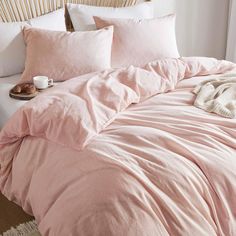 a bed with pink comforter and pillows on it next to a white rug in front of a wooden headboard