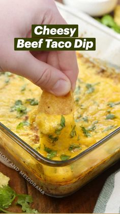 a hand dipping a tortilla chip into a casserole dish with cheese and cilantro