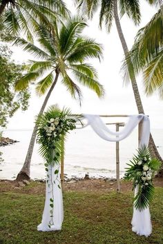 the wedding arch is decorated with greenery and white flowers for an outdoor ceremony on the beach