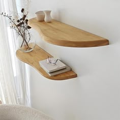 two wooden shelves on the side of a white wall next to a vase with flowers