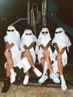 four people dressed in white sitting on a bench with their legs crossed and wearing sunglasses