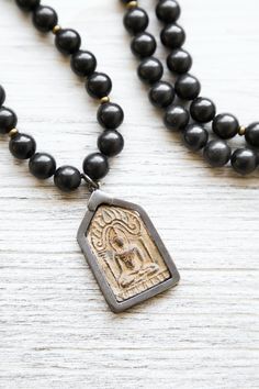 A DharmaShop exclusive 108 bead mala made from powerful, unique materials with a story! Features 108 robust Shungite beads and a handcrafted vintage Buddha protection amulet from Thailand. Shungite is known as one of the most powerful mineral healers. It has the ability to protect and purify. Black stones like Shungite are known to offer protection to the wearer, provide stability, and ground the Root Chakra. Over a decade ago, a trade with a Tibetan artifacts collector brought us these rare vin Black Gemstone Beads Mala For Healing, Handmade Black Mala For Meditation, Spiritual Obsidian Necklaces For Meditation, Handmade Black Mala As Gift, Black Spiritual Mala For Healing, Bohemian Black Mala For Healing, Black 108 Beads Mala For Meditation, Adjustable Black Spiritual Mala, Black Adjustable Spiritual Mala