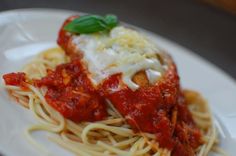 a white plate topped with spaghetti covered in tomato sauce and parmesan cheese on top