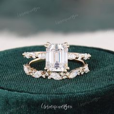 an emerald colored diamond ring sits on top of a green velvet box, with white diamonds surrounding it