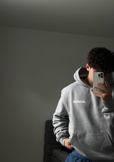 a young man taking a selfie with his cell phone in front of him while wearing sweatpants and a hoodie