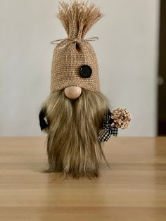 a small stuffed animal with long hair and a hat on it's head, holding a flower