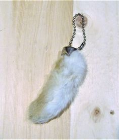 a white furry animal keychain hanging on a wooden surface with a chain attached to it