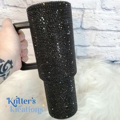 a person holding a black coffee cup covered in lots of diamonds and sparkles on their arm