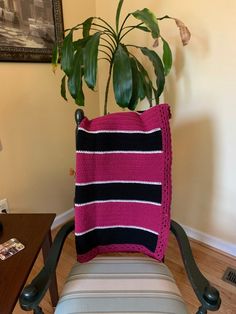 a pink and black pillow sitting on top of a chair next to a potted plant