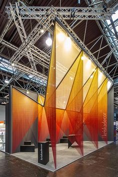 an exhibit booth with red and orange panels on the wall, lighting from overhead beams