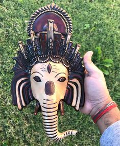 a hand holding an elephant mask in the grass