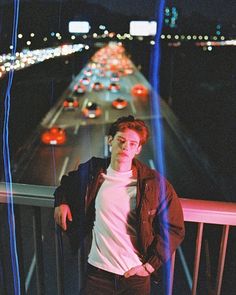 a young man standing on a bridge at night with traffic lights in the back ground