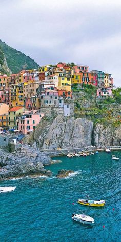 several boats floating on the water in front of some buildings and cliffs with colorfully colored houses