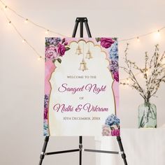 an easel with a welcome sign on it next to a vase and lights in the background