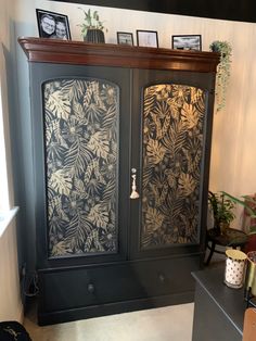 a black cabinet with leaves on it in a room next to a plant and potted plants