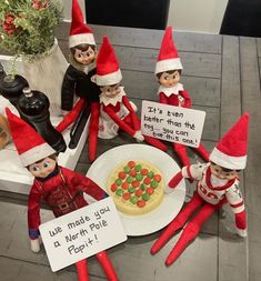 there are seven elfs sitting around a pizza on the table and one is holding a sign that says we make you a north pole for it