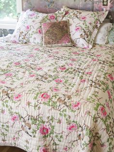 a bed with pink and green flowers on it in a bedroom next to a window