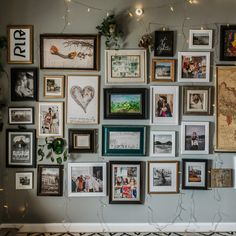 a wall with many framed pictures and lights on top of it, all hanging up against the wall