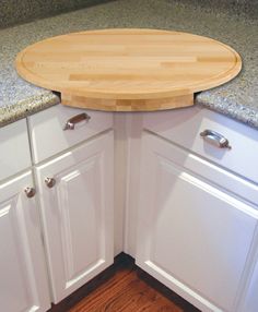 a wooden cutting board sitting on top of a kitchen counter next to white cupboards