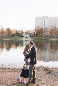 a man and woman standing next to each other in front of a lake