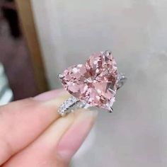 someone is holding a heart shaped pink diamond in their hand with the ring on it's finger