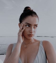 a woman in a gray dress holding her hand to her face and looking at the camera