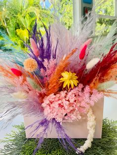 a vase filled with lots of different colored flowers and feathers on top of a table