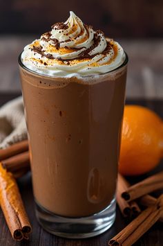 there is a drink with whipped cream and cinnamon on the table next to an orange