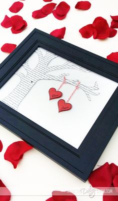 two paper hearts hanging from a string in a frame surrounded by rose petals on the floor