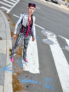 a woman standing on the side of a street next to a cross walk with graffiti