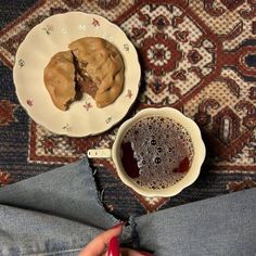 a person is sitting on the floor next to a plate with cookies and a cup of coffee