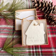 a christmas ornament in a box on a plaid blanket with pine cones and evergreen needles