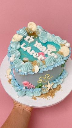 a hand is holding a cake with blue frosting and seashells on it