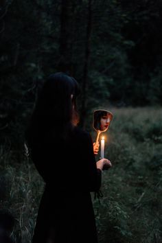 a woman holding a candle in her hand while standing in the woods at night time