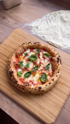 a small pizza sitting on top of a wooden cutting board next to a doughnut